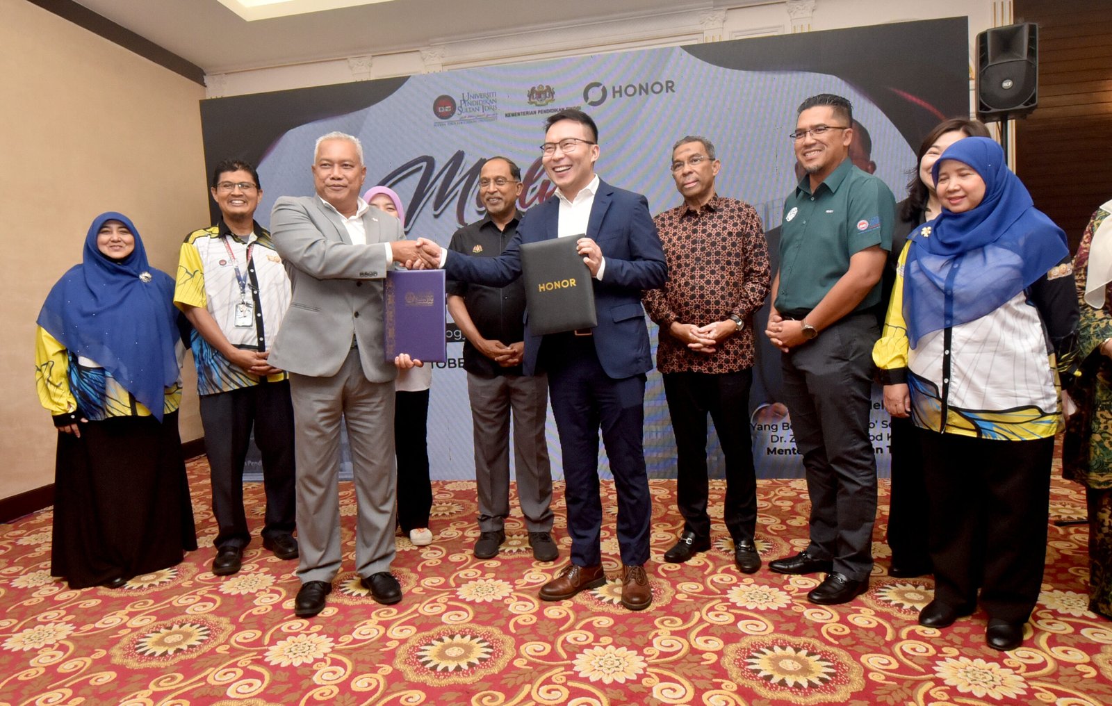 Md Amin Md Taff ( kiri) bersama Chen Long memegang dokumen MoA pada majlis pemeteraian Memorandum Perjanjian (MoA) antara UPSI dengan HONOR Technology (Malaysia) Sdn Bhd di Bilik Tetamu Utama, Dewan Tuanku Canselor, Kampus Sultan Azlan Shah UPSI sambil disaksikan oleh Zambry Abdul Kadir (tengah).